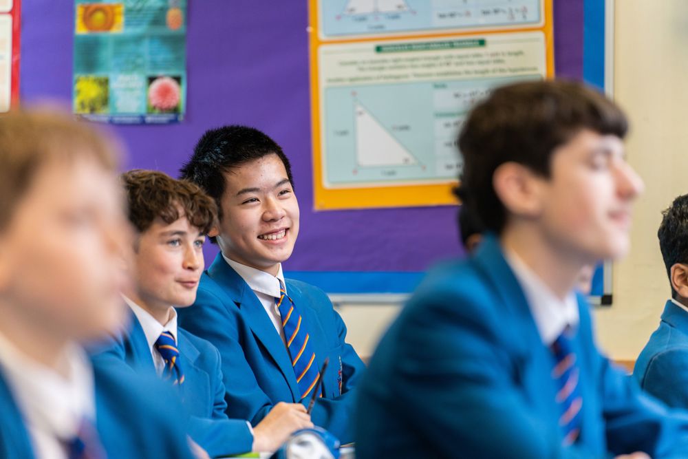 Four pupils in class, sitting in front of a Maths display board and smiling